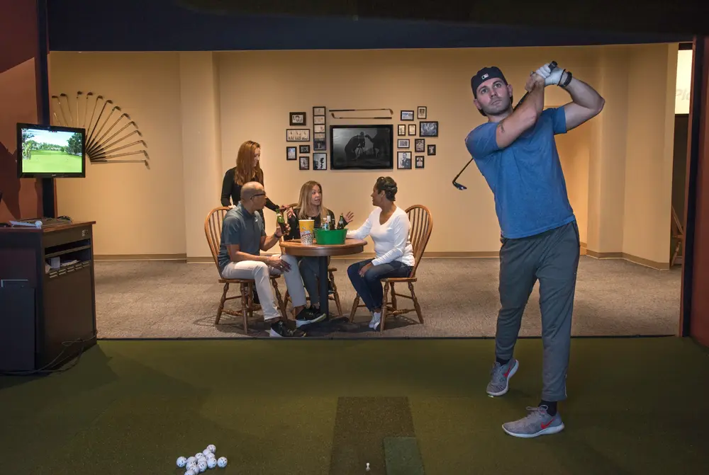A group of friends playing golf at an indoor golf simulator. One friend just finished swinging his golf club