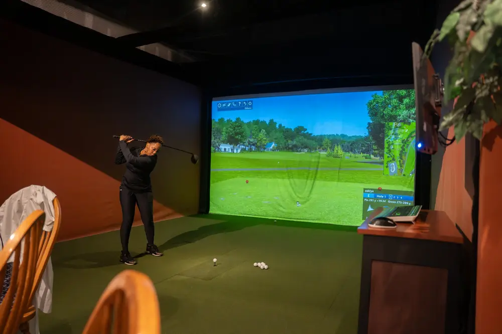 A woman swinging her golf club during a round of simulator golf
