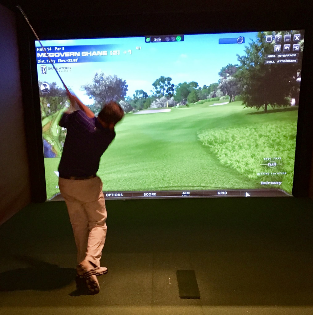 A man swinging a golf club at a golf simulator