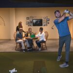 A man playing on a golf simulator a group of friends on Ardmore or Malvern, PA