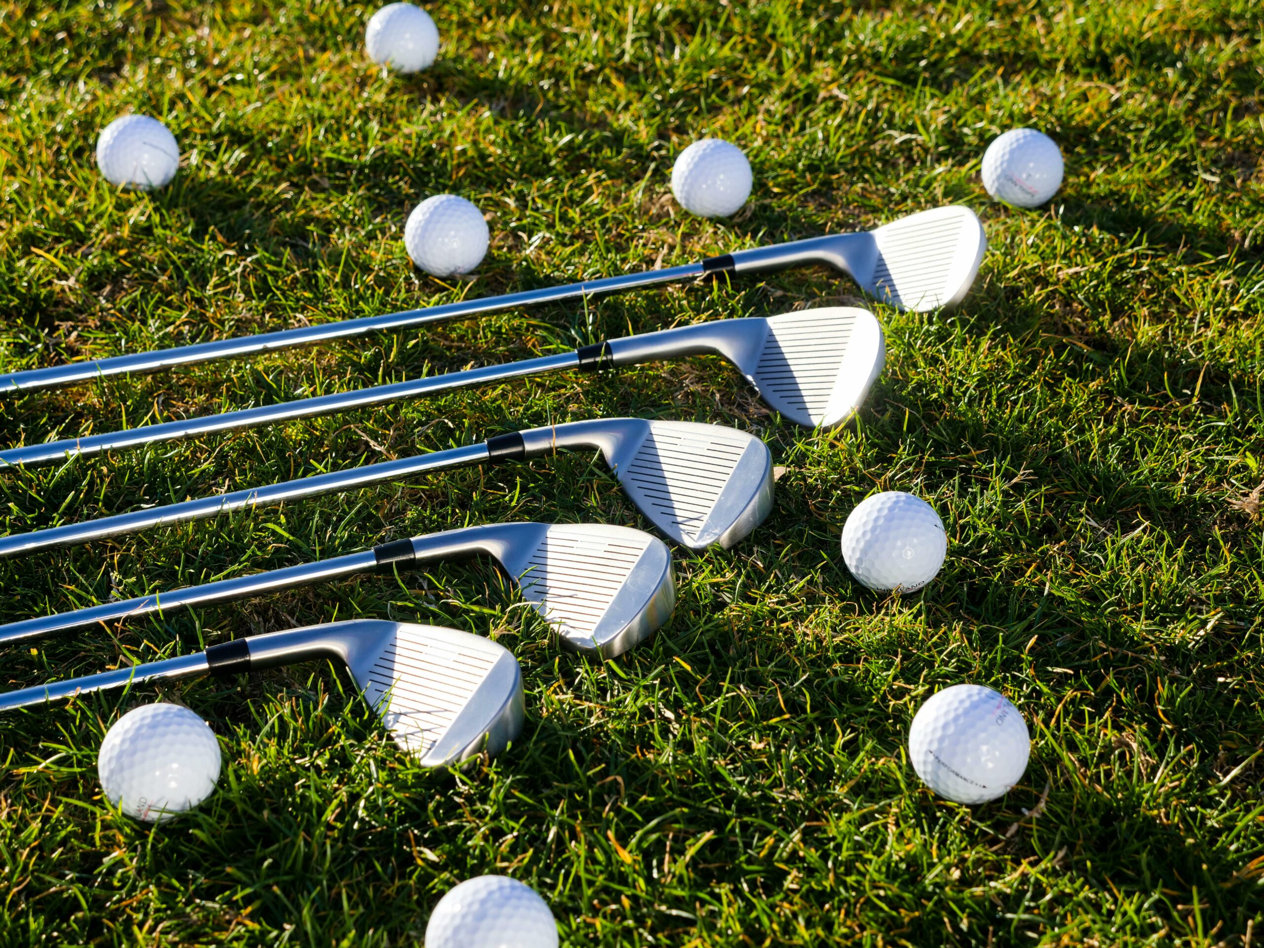 A set of irons laying on the ground surrounded by golf balls
